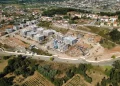 Vista dall'alto di un cantiere edile inserito nel programma portoghese delle case popolari a Coimbra, si vede un terreno piantumato e degli edifici sia in costruzione che terminati.