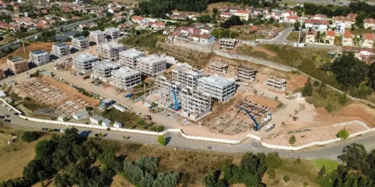 Vista dall'alto di un cantiere edile inserito nel programma portoghese delle case popolari a Coimbra, si vede un terreno piantumato e degli edifici sia in costruzione che terminati.