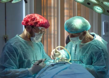 Due chirurghi in camice, mascherina e copricapo eseguono interventi chirurgici sotto le luci della ribalta. Si affidano a un efficiente sistema di prenotazione visite e chirurgia in Portogallo per garantire procedure fluide e un'assistenza mirata al paziente.