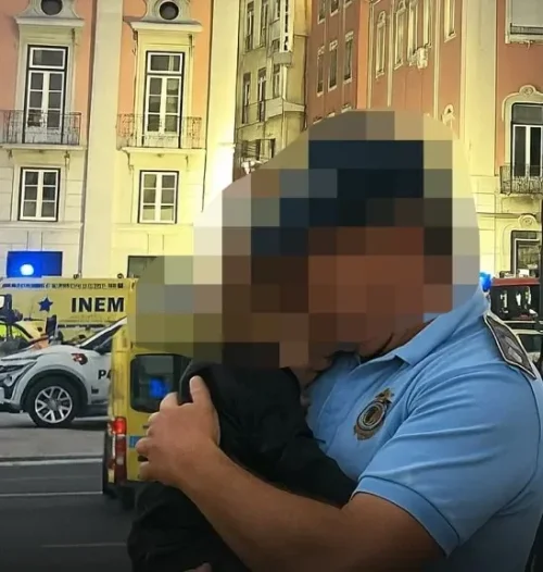 Un poliziotto abbraccia un bambino dopo la tragedia di Lisbona che ha avuto un forte impatto psicologico su tutti. La scena colta in mezzo ad una strada è pixellata per proteggere la privacy del bambino.