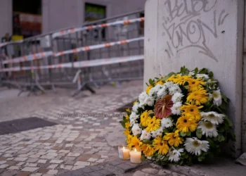 Un bouquet di fiori gialli e bianchi più due candele accese sono poste all'angolo della strada in memoria delle vittime della funicolare di Lisbona, si vedono sullo sfondo le transenne e i fettuccine della polizia.