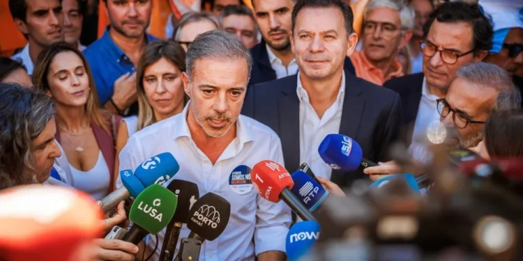 Pedro Duarte, neo eletto sindaco di Porto, in camicia bianca parla a una folla di giornalisti con microfoni colorati, con Luis Montenegro circondato da sostenitori e curiosi, con bandiere alzate sullo sfondo durante le Amministrative 2025 a Portogallo.