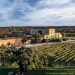 Vista aerea di una villa rustica in pietra dell'Azienda Vinicola Fitapreta di Évora, circondata da vigneti e alberi sotto un cielo parzialmente nuvoloso, con la campagna che si estende in lontananza.
