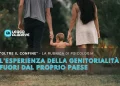 Un bambino piccolo si tiene per mano con due adulti mentre cammina all'aperto, ed il testo italiano in sovrimpressione esplora Diventare genitori all'estero e le sfide uniche della genitorialità al di fuori del proprio Paese per una rubrica di psicologia.