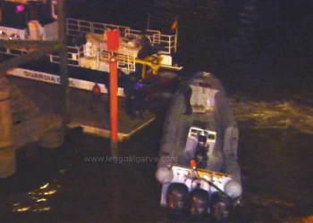 Immagine notturna con un piccolo gommone con tre motori fuoribordo, usato per il traffico di droga, è ormeggiato di notte accanto a una nave dela GUARDIA spagnola più grande, dopo che un Militare GNR è morto. A bordo ci sono delle persone e la scena poco illuminata fa pensare alla segretezza o al pericolo.