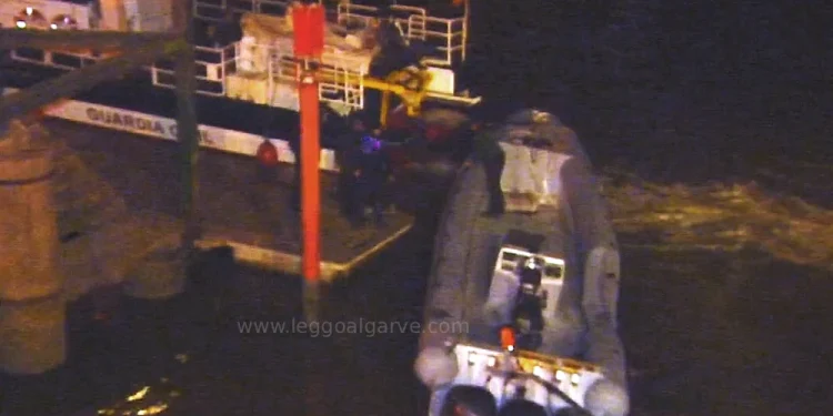 Immagine notturna con un piccolo gommone con tre motori fuoribordo, usato per il traffico di droga, è ormeggiato di notte accanto a una nave dela GUARDIA spagnola più grande, dopo che un Militare GNR è morto. A bordo ci sono delle persone e la scena poco illuminata fa pensare alla segretezza o al pericolo.