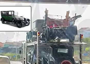 Un vettore trasporta due auto nere d'epoca, tra cui una Rolls-Royce Silver Ghost distrutta al livello superiore, con danni visibili. Un inserto rivela una chiara vista frontale dello stesso modello che guida su una strada alla luce del giorno.