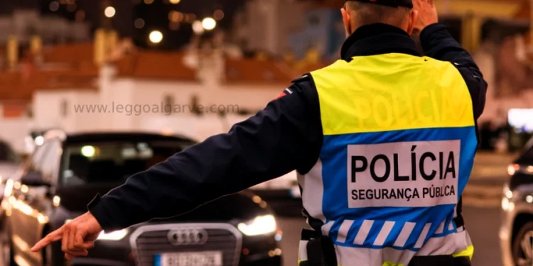Un agente di polizia che indossa un giubbotto catarifrangente con la scritta "Polícia Segurança Pública" dirige il traffico di notte, facendo segnali con un braccio mentre affronta le auto in avvicinamento, magari fermando qualcuno beccato 15 volte senza patente.