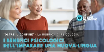 I benefici di imparare una nuova lingua dove quattro adulti anziani siedono in cerchio, sorridendo e parlando, in una stanza luminosa. Il testo in italiano evidenzia i benefici di imparare una nuova lingua per il benessere psicologico.