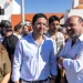 Rui Cristina eletto indaco di Albufeira con gruppo di persone all'aperto in una giornata di sole, con un uomo in camicia bianca e una donna in abito color oliva in testa, riuniti per festeggiare i risultati delle elezioni amministrative di Albufeira. Sullo sfondo sono visibili edifici bianchi e un cartello di parcheggio blu.