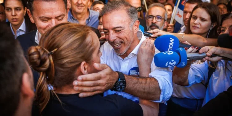 Pedro Duarte sorridente tra la folla stringe la mano e viene abbracciato da un sostenitore dopo la vittoria delle elezioni amministrative di Porto, circondato dalla gente e dai microfoni dei giornalisti in un vivace evento pubblico.