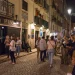 Una folla vivace si raduna di notte fuori da un pub irlandese su una strada acciottolata del Bairro Alto di Lisbona; le persone chiacchierano, stanno in piedi e si siedono, mentre gli edifici illuminati dai lampioni vantano balconi e bandiere, spesso poi restano scene di degrado.