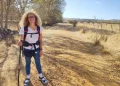 Silvana Di Liberto con i capelli ricci e gli occhiali si accovaccia e sorride all'obiettivo su un sentiero lungo la Via de la Plata, in Castilla y Leon. Sullo sfondo, alcuni alberi, delle colline e un cielo azzurro.