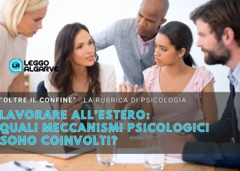 Un gruppo eterogeneo di quattro professionisti siede intorno a un tavolo per discutere, con documenti e un computer portatile visibili. All'immagine si sovrappone un titolo italiano sul lavoro estero e sui meccanismi psicologici.