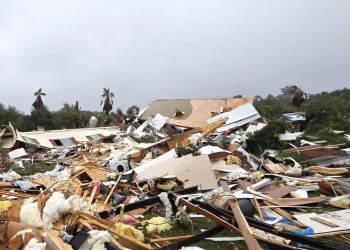 I detriti dei bungalow distrutti sono sparsi sul terreno dopo un tornado in un campeggio di Albufeira in Portogallo, evidenziando il pericolo, tra alberi caduti e cielo nuvoloso sullo sfondo.