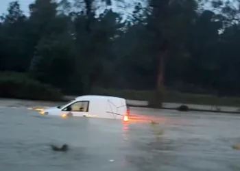 Un auto bianca sommersa dall'acqua a causa della pioggia e del maltempo in Portogallo, sullo sfondo una folta vegetazione di alberi.