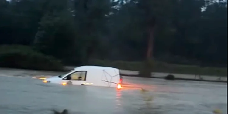 Un auto bianca sommersa dall'acqua a causa della pioggia e del maltempo in Portogallo, sullo sfondo una folta vegetazione di alberi.