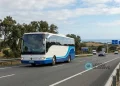 Un pullman bianco e blu, percorre in sicurezza un'autostrada in Portogallo con alberi e colline sullo sfondo. I cartelli stradali indicano Algarve e Lisbona sotto un cielo parzialmente nuvoloso.