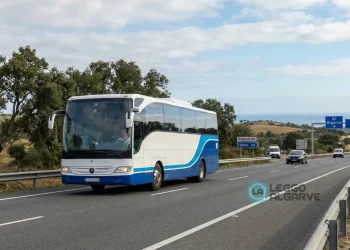 Un pullman bianco e blu, percorre in sicurezza un'autostrada in Portogallo con alberi e colline sullo sfondo. I cartelli stradali indicano Algarve e Lisbona sotto un cielo parzialmente nuvoloso.