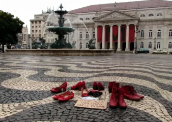 Le scarpe rosse, simbolo della lotta alla violenza contro le donne, sono disposte in una piazza di Lisbona in Portogallo vicino a un cartello con una scritta, davanti al Teatro Nazionale Dona Maria II, con colonne e striscioni rossi, accanto a una grande fontana.