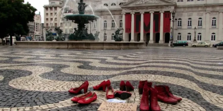 Le scarpe rosse, simbolo della lotta alla violenza contro le donne, sono disposte in una piazza di Lisbona in Portogallo vicino a un cartello con una scritta, davanti al Teatro Nazionale Dona Maria II, con colonne e striscioni rossi, accanto a una grande fontana.