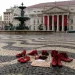 Le scarpe rosse, simbolo della lotta alla violenza contro le donne, sono disposte in una piazza di Lisbona in Portogallo vicino a un cartello con una scritta, davanti al Teatro Nazionale Dona Maria II, con colonne e striscioni rossi, accanto a una grande fontana.