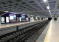La stazione della metropolitana di Santa Apolónia, prima della chiusuara, pulita e moderna, con banchine vuote, pavimenti piastrellati e manifesti pubblicitari alle pareti. I binari corrono al centro, mentre le luminose luci del soffitto illuminano l'ampia area.