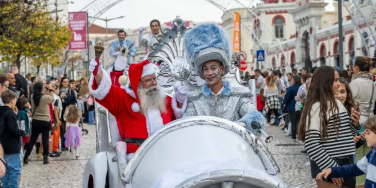 Babbo Natale e una persona con un costume d'argento lucido viaggiano su un'auto bianca durante la parata di Natale a Loulé in Algarve, circondati dalla folla e da bambini che guardano e scattano foto. Decorazioni ed edifici fanno da sfondo.