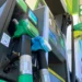 Vista ravvicinata di due erogatori di carburante - uno verde e uno blu - presso una stazione di servizio, con i numeri delle pompe e parte della tettoia sotto un cielo limpido, in mezzo alle discussioni in corso su Tasse carburanti Portogallo.