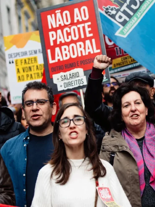 Un gruppo di persone manifestano a Lisbona per lo sciopero generale in Portogallo, sfilando con cartelli con le scrite "PACOTE LABORAL" nel mezzo dei palazzi di Lisbona.