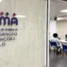 Una persona siede in un'area d'attesa dell'ufficio dell'Agência para a Integração Migrações e Asilo (AIMA), in attesa del proprio turno per l'aggiornamento dati utenti AIMA, con banchi di servizio numerati e una parete di vetro con il nome e il logo dell'agenzia.