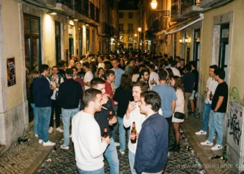 Una folla di giovani si riunisce durante la movida notturna a Lisbona, dove in alcune zone sono vietati alcolici consumati in strada, mentre sorseggiano birre e chiacchierano tra i vicoli storici del Bairro Alto caratterizzati da graffiti e sampietrini.