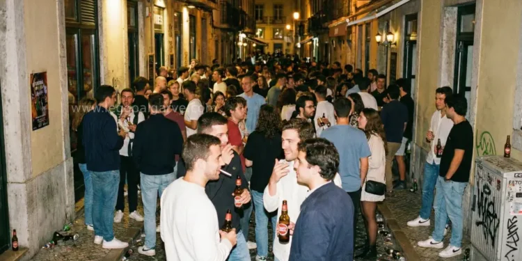Una folla di giovani si riunisce durante la movida notturna a Lisbona, dove in alcune zone sono vietati alcolici consumati in strada, mentre sorseggiano birre e chiacchierano tra i vicoli storici del Bairro Alto caratterizzati da graffiti e sampietrini.