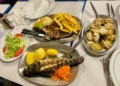 Una tavola di un ristorante in Portogallo con piatti di pesce grigliato, carne, patatine fritte, riso e insalata, che illustra la ricca cultura culinaria locale nonostante le difficoltà economiche della crisi ristoranti portoghesi.
