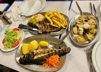 Una tavola di un ristorante in Portogallo con piatti di pesce grigliato, carne, patatine fritte, riso e insalata, che illustra la ricca cultura culinaria locale nonostante le difficoltà economiche della crisi ristoranti portoghesi.