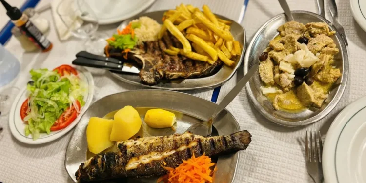 Una tavola di un ristorante in Portogallo con piatti di pesce grigliato, carne, patatine fritte, riso e insalata, che illustra la ricca cultura culinaria locale nonostante le difficoltà economiche della crisi ristoranti portoghesi.