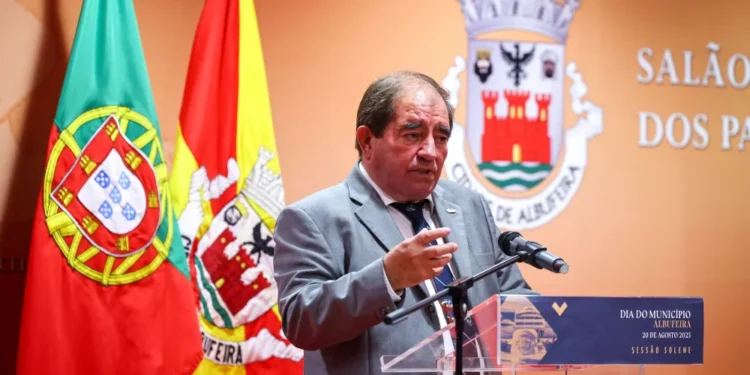 Una foto del ex-sindaco José Carlos Rolo morto a seguito di una complicazione, ha giacca e cravatta, parla ad un microfono difronte alle bandiere di Albufeira.