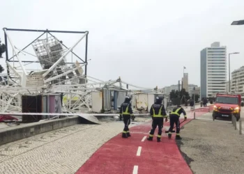 In una strada cittadina i vigili del fuoco lavorano ai danni causati dalla pioggia e dal maltempo in Portogallo, dove un impalcatura è crollata in mezzo ad una pista ciclabile di colore rosso.