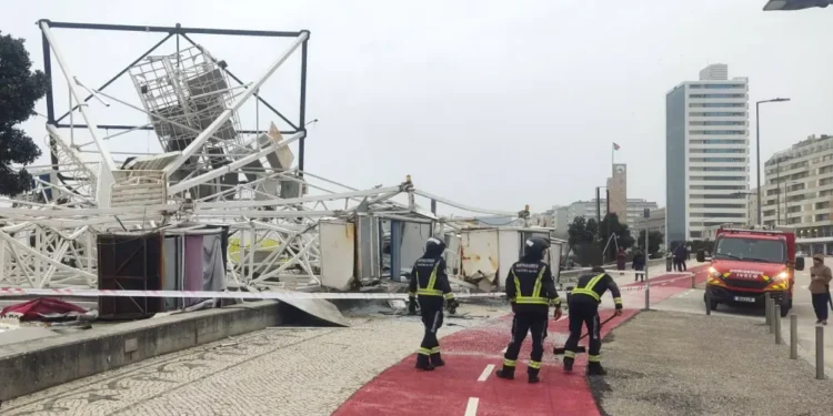 In una strada cittadina i vigili del fuoco lavorano ai danni causati dalla pioggia e dal maltempo in Portogallo, dove un impalcatura è crollata in mezzo ad una pista ciclabile di colore rosso.