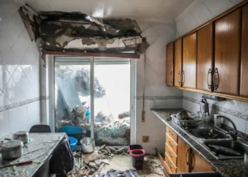 Una cucina con gravi danni; parte del soffitto e della parete sono crollati, i detriti sono sparsi sul pavimento e gli oggetti della cucina sono disordinati. La luce entra dalle porte scorrevoli in vetro, evidenziando la necessità di una ricostruzione dopo il passaggio in Portogallo della tempesta Kristin.