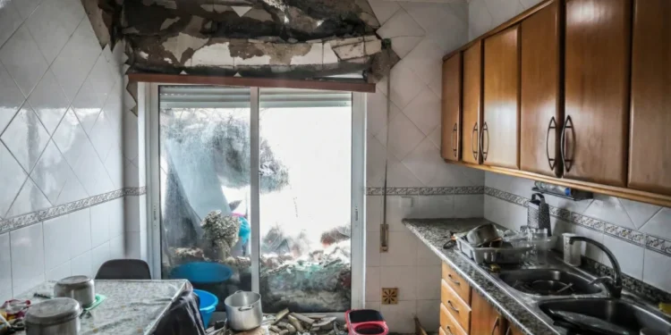 Una cucina con gravi danni; parte del soffitto e della parete sono crollati, i detriti sono sparsi sul pavimento e gli oggetti della cucina sono disordinati. La luce entra dalle porte scorrevoli in vetro, evidenziando la necessità di una ricostruzione dopo il passaggio in Portogallo della tempesta Kristin.