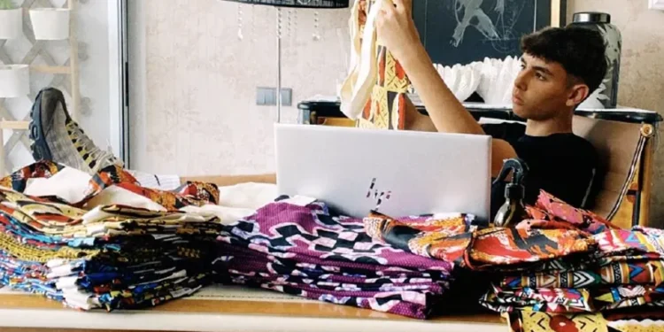 Duarte Silva immagine e osserva le sue borse colorate Capubag, con molti tessuti colorati sulla scrivana ed un pc.