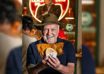 Luis Bosco sorridente tiene tra le mani un panino con cotoletta gigante, all'interno del suo locale di Porto.