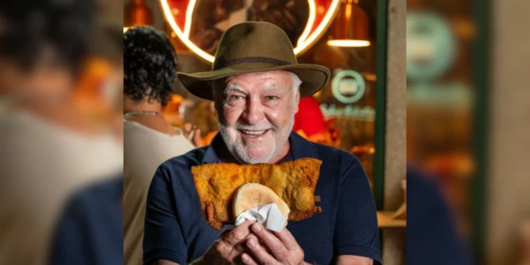 Luis Bosco sorridente tiene tra le mani un panino con cotoletta gigante, all'interno del suo locale di Porto.