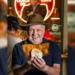 Luis Bosco sorridente tiene tra le mani un panino con cotoletta gigante, all'interno del suo locale di Porto.
