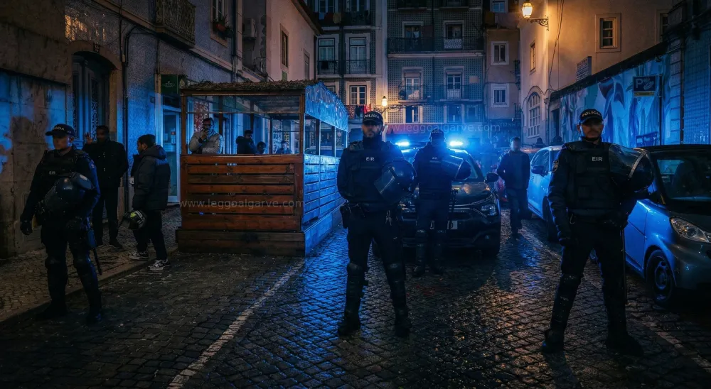 Rua do Benformoso a Lisbona di notte con quattro agenti di polizia, luogo dellas cena di un crimine legato ai cartelli del narcotraffico a Lisbona. Si vedono palazzi, alcune persone sul ciglio della strada e un auto  con i lampeggianti azzurri accessi.
