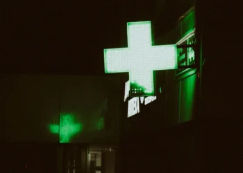 L'insegna verde di una farmacia dove è possibile eseguire un Test HIV a Lisbona. Immagine notturna con una croce verde a led.