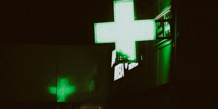 L'insegna verde di una farmacia dove è possibile eseguire un Test HIV a Lisbona. Immagine notturna con una croce verde a led.