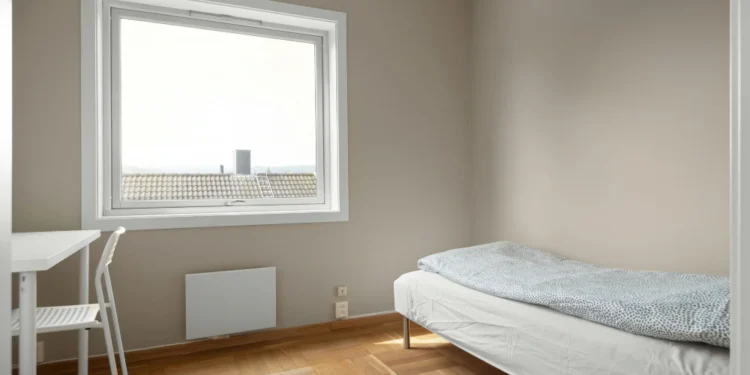 Una camera minimal con pareti beige chiaro, un letto singolo con piumone a pois, una scrivania e una sedia bianche, parquet in legno e un'ampia finestra che lascia entrare la luce naturale: l'ideale per chi vuole affittare stanze Portogallo.