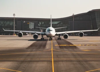 Un grande aereo commerciale, sostenuto da efficienti scorte di carburante aereo, è posizionato sulla pista rivolto in avanti, con un moderno edificio del terminal aeroportuale sullo sfondo sotto un cielo limpido.